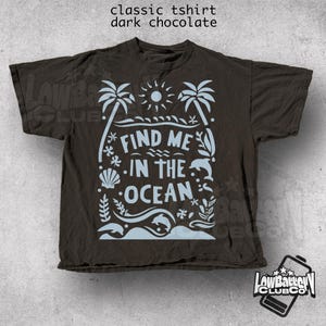 Puede incluir: Camiseta cl&aacute;sica de color chocolate oscuro con un dise&ntilde;o de tem&aacute;tica oce&aacute;nica en azul claro. El dise&ntilde;o incluye palmeras, un sol, olas, un delf&iacute;n y el texto "FIND ME IN THE OCEAN". La camiseta es de Low Battery Club Co.