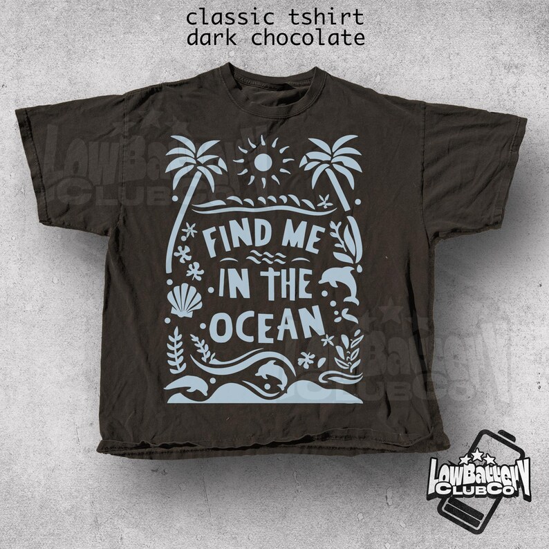 Puede incluir: Camiseta cl&aacute;sica de color chocolate oscuro con un dise&ntilde;o de tem&aacute;tica oce&aacute;nica en azul claro. El dise&ntilde;o incluye palmeras, un sol, olas, un delf&iacute;n y el texto "FIND ME IN THE OCEAN". La camiseta es de Low Battery Club Co.