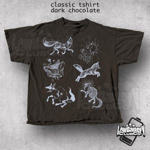 May include: Dark chocolate-colored classic t-shirt with white illustrations of foxes and suns. The shirt features the text "classic tshirt dark chocolate" at the top. The shirt has a relaxed fit and a logo in the bottom right corner.
