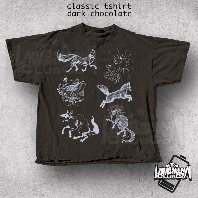 May include: Dark chocolate-colored classic t-shirt with white illustrations of foxes and suns. The shirt features the text "classic tshirt dark chocolate" at the top. The shirt has a relaxed fit and a logo in the bottom right corner.