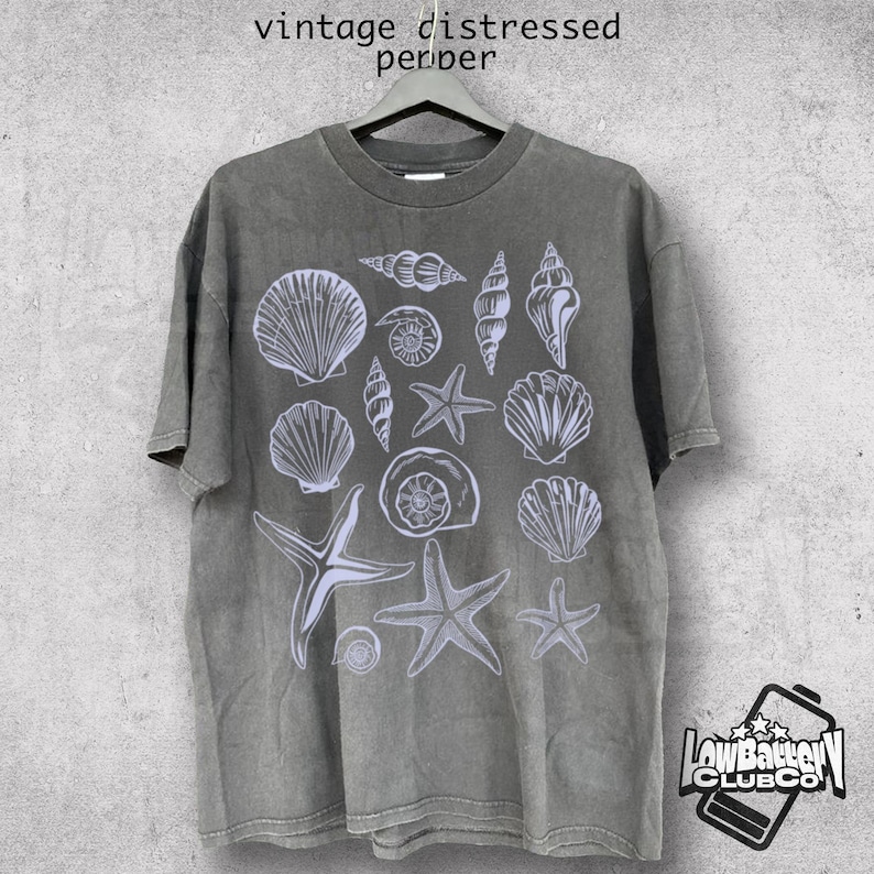 May include: A gray, vintage-style t-shirt featuring a white illustration of various seashells and starfish. The shirt has a distressed look, with the words "vintage distressed pepper" printed at the top. The shirt is hanging on a hanger.