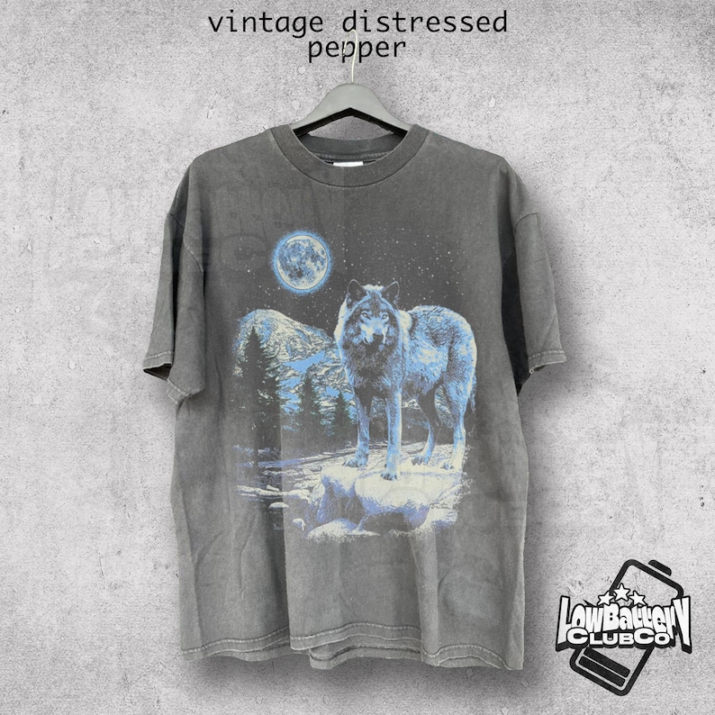 May include: Vintage distressed gray t-shirt featuring a wolf howling at the moon with a mountain range in the background. The shirt has a faded look and a distressed feel.