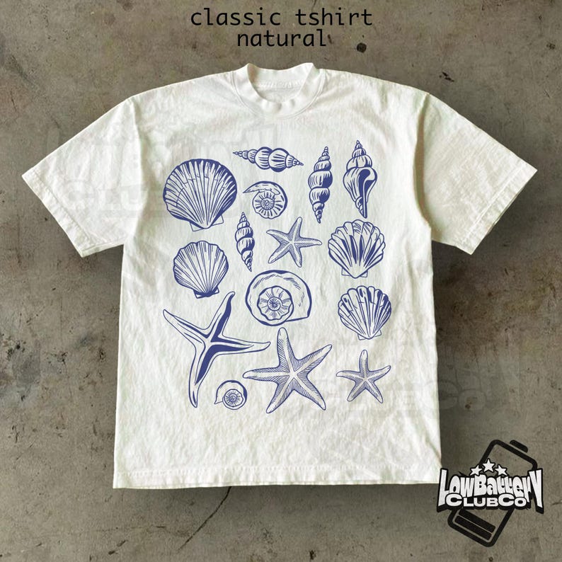 May include: A white t-shirt with a crew neck featuring a blue illustration of various seashells and starfish. The text "classic tshirt natural" is printed at the top. The shirt has short sleeves and a relaxed fit.