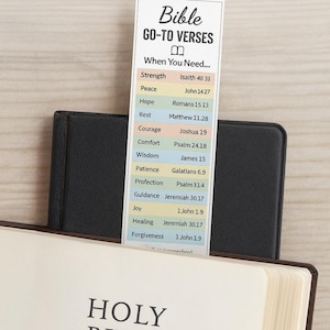 Peut inclure: Un marque-page imprimable avec "Bible GO-TO VERSES" et des versets pour différents besoins. Le marque-page est inséré dans un livre noir, avec les mots "HOLY BIBLE" visibles.
