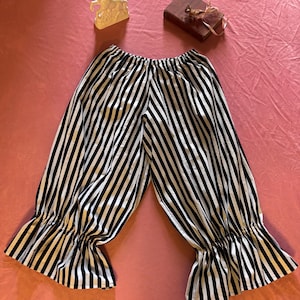 May include: Loose-fitting pants featuring a vertical black and white striped pattern. The garment has an elasticized waistband and gathered, ruffled cuffs at the bottom of each leg, creating a voluminous silhouette with a distinct striped design.