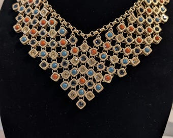 Colar babador geométrico dourado assinado pela Chico's, com colar statement em turquesa, laranja e azul com strass.