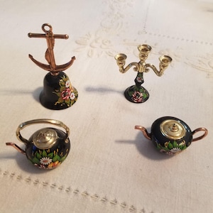 May include: A set of miniature decorative items, including a bell with an anchor, a three-arm candelabra, and two small teapots. The items are black with floral designs and gold accents. The bell is approximately 5 cm tall.