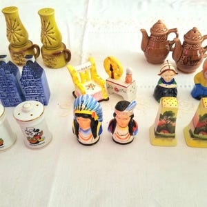 Può includere: Una collezione di saliere e pepiere vintage in varie forme e design. Include case olandesi, figure di nativi americani, teiere e saliere gialle con dipinti di paesaggi. Le saliere sono in ceramica.