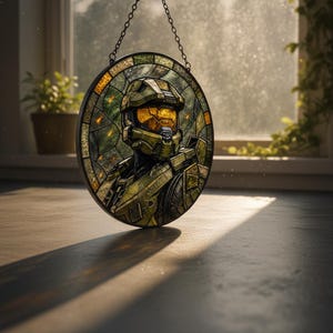 May include: Circular stained glass panel depicting a character in green and gold armour. The artwork is suspended by a chain. The panel is set against a window with natural light.