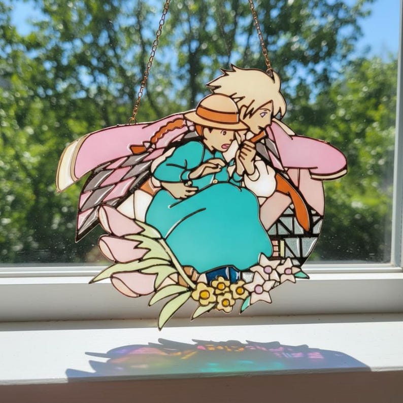 May include: Stained glass art piece featuring a scene from a popular animated film. The artwork depicts two characters in a loving embrace, surrounded by floral elements. The piece is primarily pink, teal, and beige, with a copper chain for hanging.