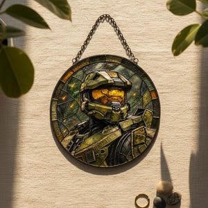 May include: Circular stained glass artwork depicting a character in green and gold armour and helmet. The piece is framed and hangs from a chain. The background features green and orange hues, creating a striking visual.