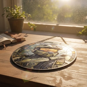 May include: Circular stained glass artwork depicting a character from the Halo video game series. The design features the character's helmet and armour in green, gold, and grey, with a chain for hanging. The artwork is approximately 20 cm in diameter.