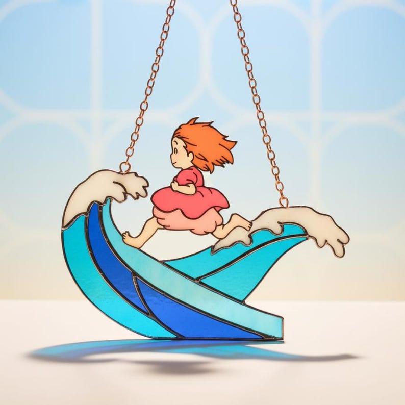 May include: Stained glass suncatcher featuring a cartoon girl with red hair and a pink dress running on a blue and white wave. The suncatcher is suspended by copper-colored chains. The background is a light blue.