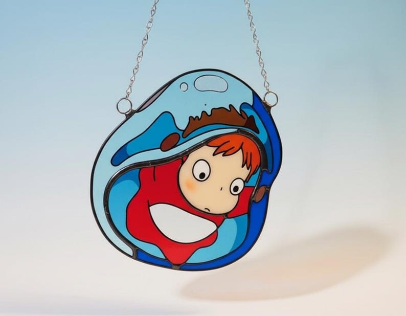 May include: Stained glass suncatcher featuring a cartoon character in a red outfit, surrounded by blue water. The artwork is outlined in black and hangs from a silver chain. The character has large eyes and orange hair.