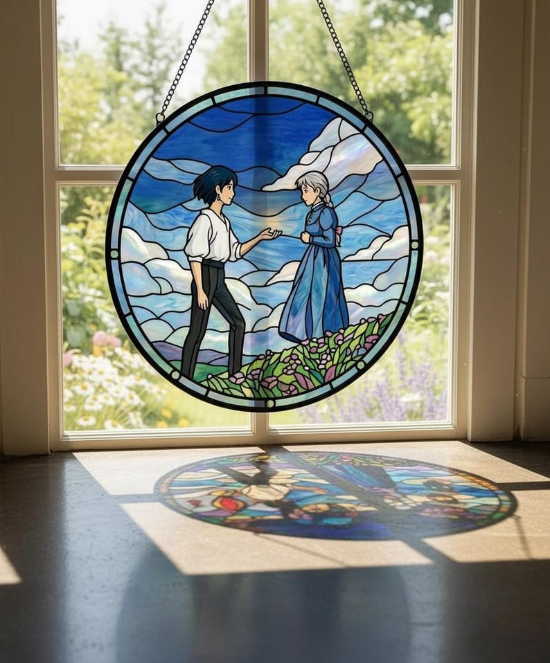 May include: Round stained glass window art featuring a scene with two figures in a blue sky and cloud background. The artwork is framed in black and suspended by a chain. The image casts a circular shadow on the floor.