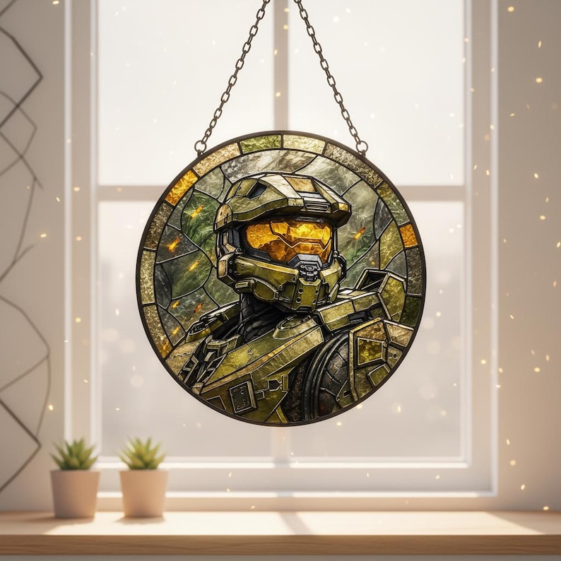 May include: A circular stained glass panel depicting a character in green armour. The artwork is suspended by a chain and set against a window. The character's visor glows with a warm, golden light, set against a backdrop of green.