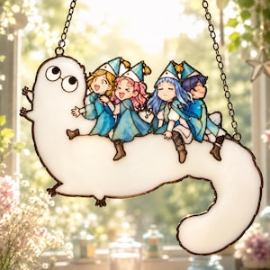 May include: A stained glass window hanging featuring a white, worm-like creature with large eyes, carrying four anime-style figures. The figures wear blue robes and hats. The window is outlined in a dark brown and hangs from a chain.