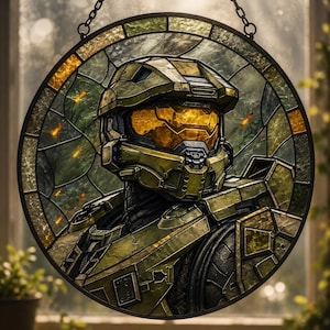 May include: Circular stained glass artwork depicting a futuristic soldier in olive green armour. The soldier's helmet has a gold visor. The glass is framed in a dark metal and hangs from a chain. The background shows a blurred outdoor scene.