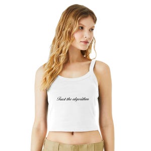 Puede incluir: Top corto blanco con cuello redondo y tirantes finos. El texto "Trust the algorithm" está impreso en escritura negra en la parte delantera. La parte superior está hecha de un material suave y ligero.