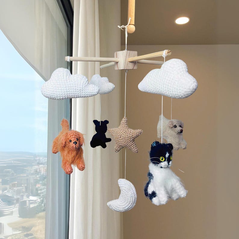 May include: A hanging mobile featuring a wooden cross frame with white crocheted clouds, a beige crocheted star, a white crocheted crescent moon, and several plush animal figures including a brown dog, a black dog silhouette, and a cat.