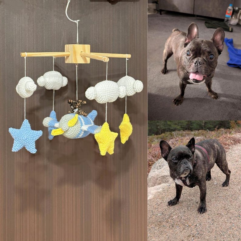 Puede incluir: Un m&oacute;vil de ganchillo con marco de madera, nubes blancas, estrellas amarillas y un avi&oacute;n azul y amarillo con una peque&ntilde;a figura de perro marr&oacute;n. El m&oacute;vil est&aacute; suspendido por un hilo blanco sobre una superficie vertical marr&oacute;n oscuro.