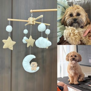May include: A nursery mobile featuring a light wooden cross frame with hanging crocheted elements including two beige stars, two light blue clouds, two light blue spheres, and a light blue crescent moon with a small beige crocheted dog figure.