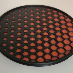 May include: A round coaster with a honeycomb pattern in black and orange. The honeycomb pattern is black on the left side and orange on the right side.