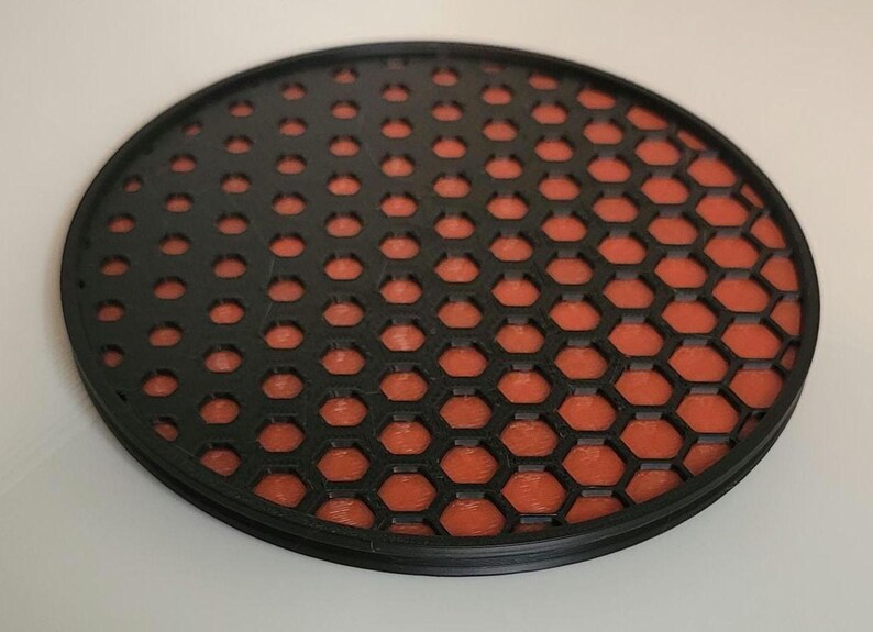 May include: A round coaster with a honeycomb pattern in black and orange. The honeycomb pattern is black on the left side and orange on the right side.