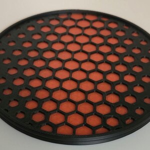 May include: A round black coaster with a honeycomb pattern. The honeycomb is orange and black.