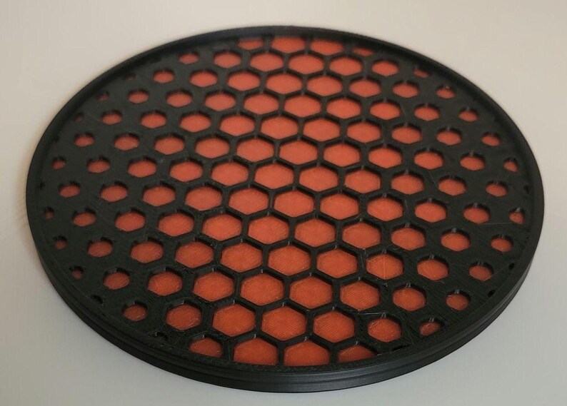 May include: A round black coaster with a honeycomb pattern. The honeycomb is orange and black.