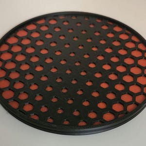 May include: A round black coaster with a honeycomb pattern. The honeycomb pattern is orange.