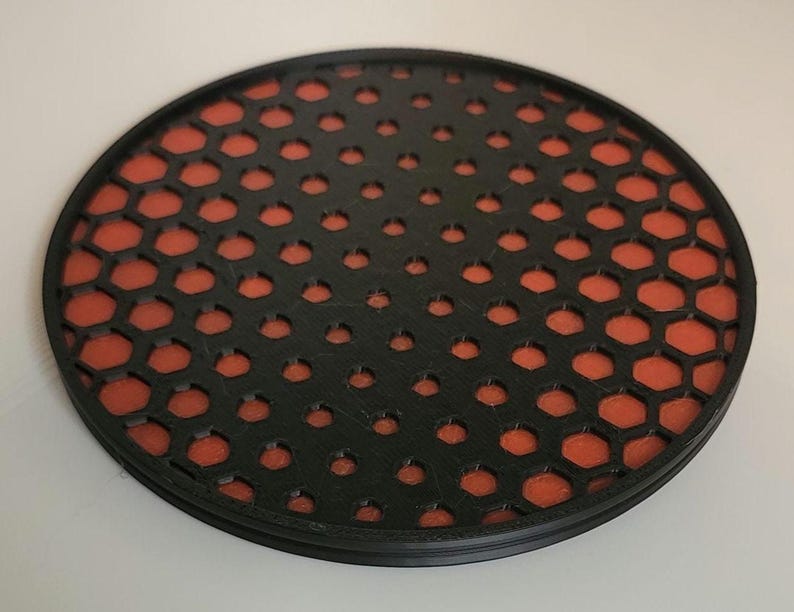 May include: A round black coaster with a honeycomb pattern. The honeycomb pattern is orange.