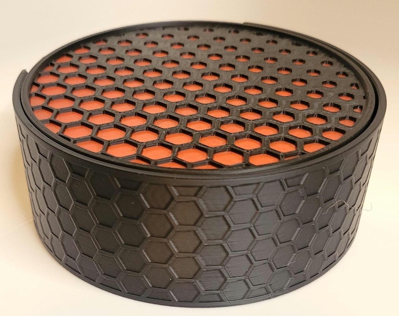 May include: A black round container with a honeycomb pattern on the outside and a red honeycomb pattern on the lid.