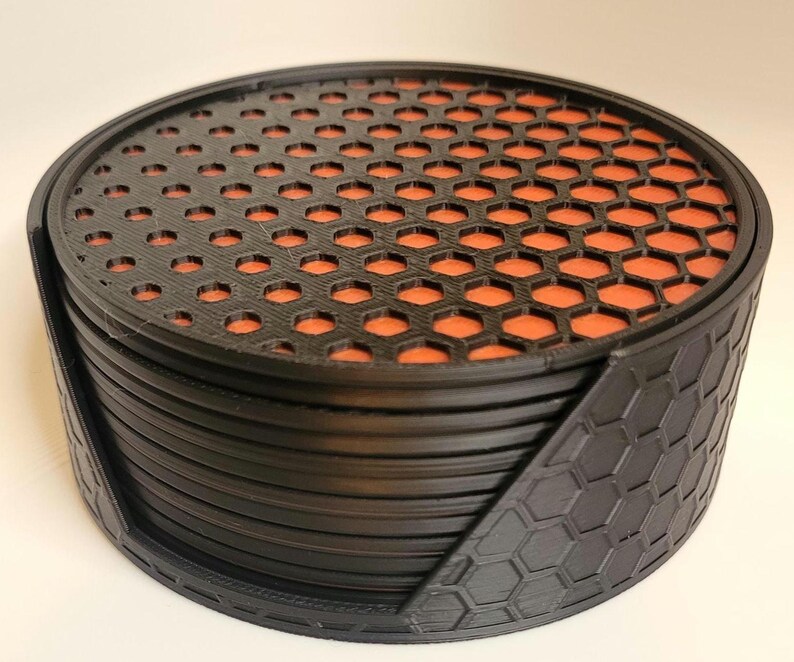 May include: A set of black and orange coasters with a honeycomb pattern. The coasters are stacked in a circular holder.