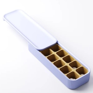 May include: A rectangular ice cube tray with a light purple exterior and a gold-colored interior. The tray has a lid and is divided into ten square compartments. The lid is partially open, revealing the compartments.