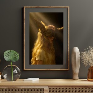 Può includere: Una stampa artistica incorniciata raffigurante una persona con lunghi capelli biondi che indossa un elmo alato color oro. L'opera d'arte è illuminata da un raggio di luce, creando un effetto drammatico. La cornice è di colore marrone caldo.