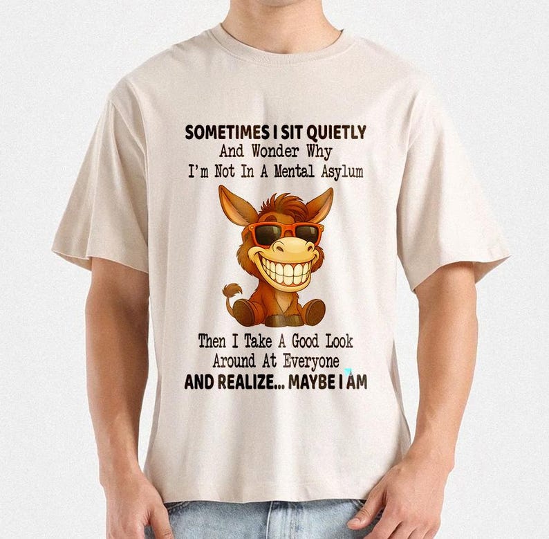 Puede incluir: Camiseta beige con un burro de dibujos animados con gafas de sol y una gran sonrisa. La camiseta tiene el texto: "SOMETIMES I SIT QUIETLY And Wonder Why I'm Not In A Mental Asylum Then I Take A Good Look Around At Everyone AND REALIZE... MAYBE I AM."