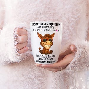 Puede incluir: Taza de cer&aacute;mica blanca con un burro de dibujos animados con gafas de sol y una gran sonrisa. La taza tiene el texto "SOMETIMES I SIT QUIETLY And Wonder Why I'm Not In A Mental Asylum Then I Take A Good Look Around At Everyone AND REALIZE... MAYBE I AM."