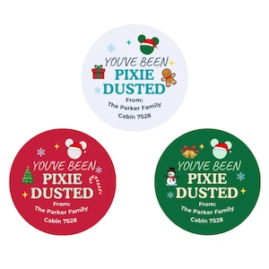 May include: Three circular stickers with holiday themes. The top sticker is white with a gingerbread man, gift, and mouse ears. The bottom left is red with a tree and candy cane. The bottom right is green with a snowman and bells. All feature the text YOU'VE BEEN PIXIE DUSTED From: The Parker Family Cabin 7528.