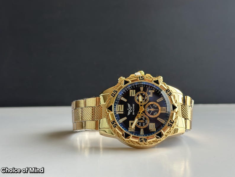 May include: A gold-toned wristwatch with a black and blue face. The watch features a textured gold band and a detailed bezel. The watch face displays multiple subdials and gold-colored hands and markers. The text "ZHONE" is visible on the watch face. The text "Choice of Mind" is visible at the bottom.