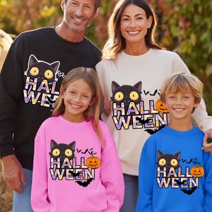 Op de afbeelding: Een familie draagt Halloween-sweatshirts. De sweatshirts zijn zwart, crème, roze en blauw, elk met een zwarte kat, het woord "Halloween", een pompoen en vleermuizen. De familie lacht.