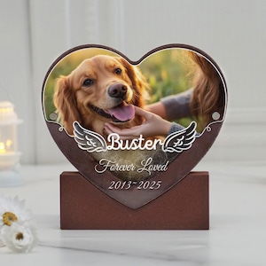 Może przedstawiać: Pamiątkowa tablica w kształcie serca z golden retrieverem o imieniu Buster. Tablica zawiera napis "Buster Forever Loved 2013-2025" i dekoracyjne skrzydła anioła. Tablica jest zamontowana na brązowym stojaku.