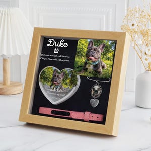 May include: A wooden framed pet memorial with a photo of a French Bulldog named Duke, a heart-shaped photo with angel wings, and a pink dog collar. The frame includes the text "Duke" and a paw print.