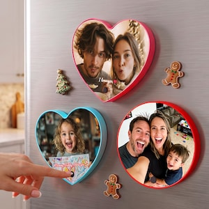 May include: Three magnetic photo frames in heart and circular shapes with red and blue borders. The frames display personal photographs, including one with the text I love you. Two small gingerbread man and Christmas tree magnets are included.