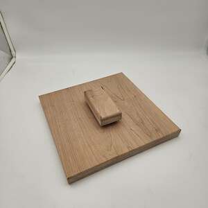 May include: A light brown wooden cutting board with a rectangular shape. A smaller, rectangular wooden piece is attached to the board. The wood grain is visible. The cutting board is likely used for food preparation.