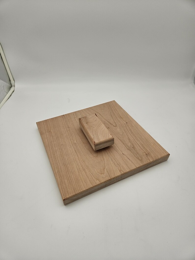 May include: A light brown wooden cutting board with a rectangular shape. A smaller, rectangular wooden piece is attached to the board. The wood grain is visible. The cutting board is likely used for food preparation.