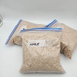 Puede incluir: Tres bolsas de pl&aacute;stico transparente llenas de virutas de madera de color marr&oacute;n claro. La bolsa de la parte delantera tiene una etiqueta blanca que dice "MAPLE" en rotulador negro. Las bolsas tienen cierres de cremallera azules y blancos.