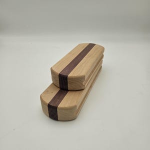 May include: Two wooden boxes with a light wood exterior and a dark brown stripe down the center. The boxes are rectangular with rounded edges. One box is stacked on top of the other.