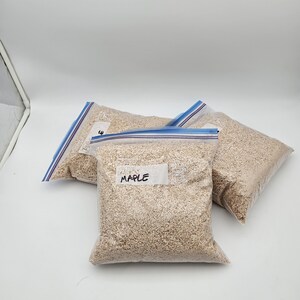 Puede incluir: Tres bolsas de pl&aacute;stico transparente llenas de material marr&oacute;n claro, posiblemente virutas o virutas de madera, est&aacute;n dispuestas sobre una superficie blanca. Una bolsa tiene una etiqueta que dice "MAPLE". Las bolsas est&aacute;n selladas con cierres de cremallera azules.