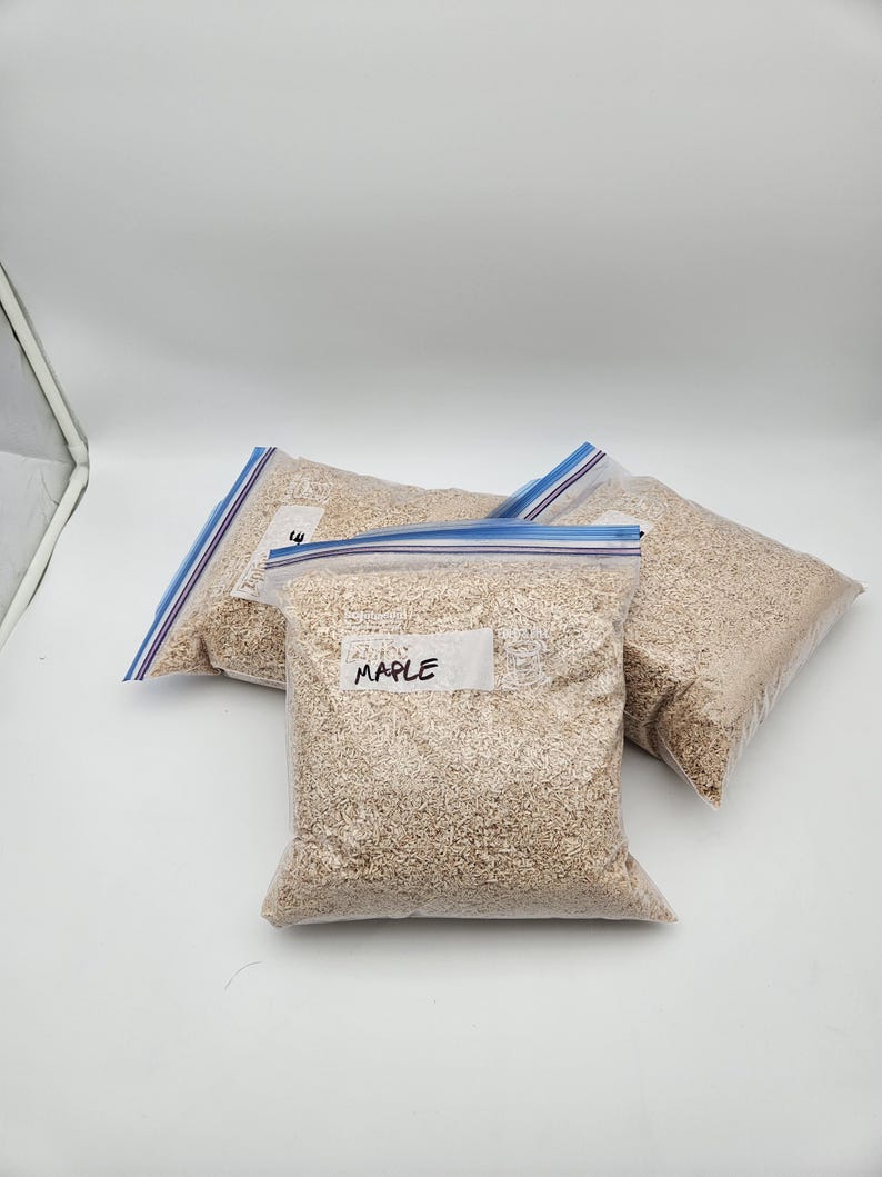 Puede incluir: Tres bolsas de pl&aacute;stico transparente llenas de material marr&oacute;n claro, posiblemente virutas o virutas de madera, est&aacute;n dispuestas sobre una superficie blanca. Una bolsa tiene una etiqueta que dice "MAPLE". Las bolsas est&aacute;n selladas con cierres de cremallera azules.